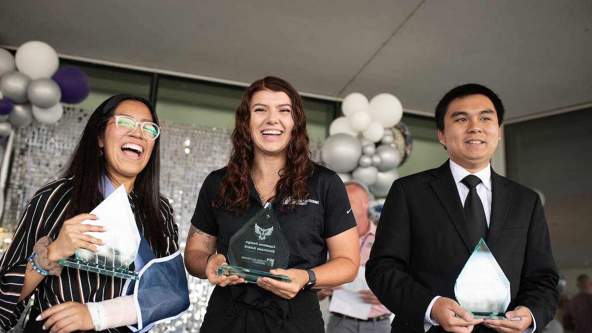 three former students holding awards