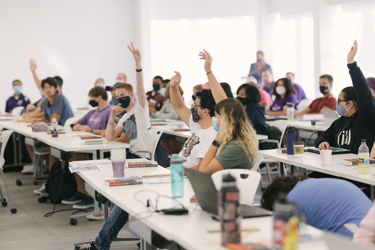 Students in a classroom with their hands raised.